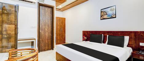 A hotel room with a bed, a desk, a chair, a ceiling fan, and a painting on the wall.