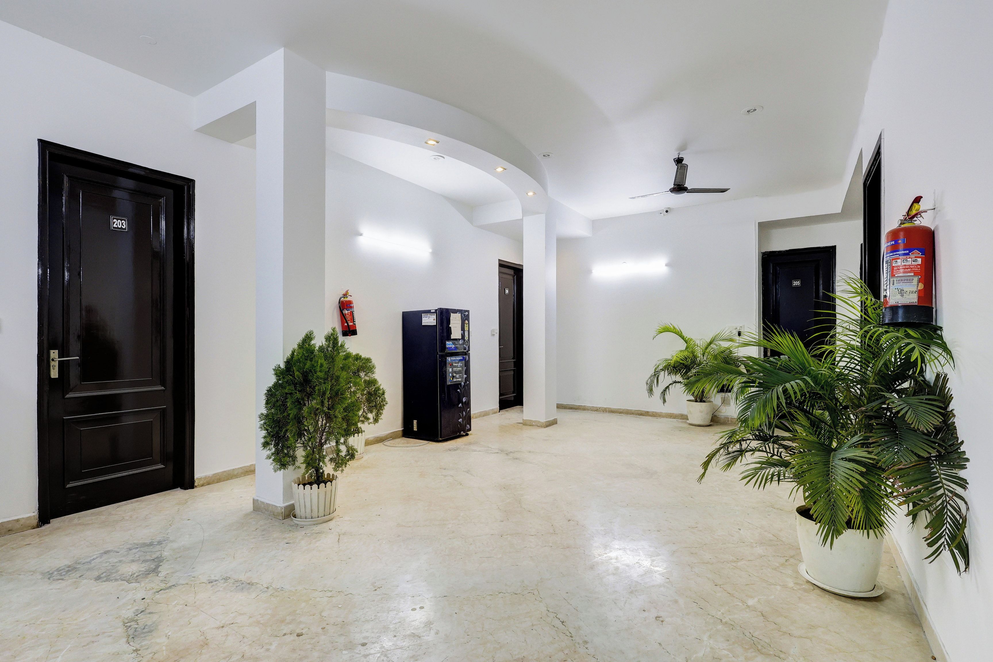 A hallway with a marble floor, black doors, and potted plants.