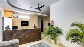Un espace d’accueil avec un comptoir en bois, une horloge, une statue de Bouddha et des plantes en pot.