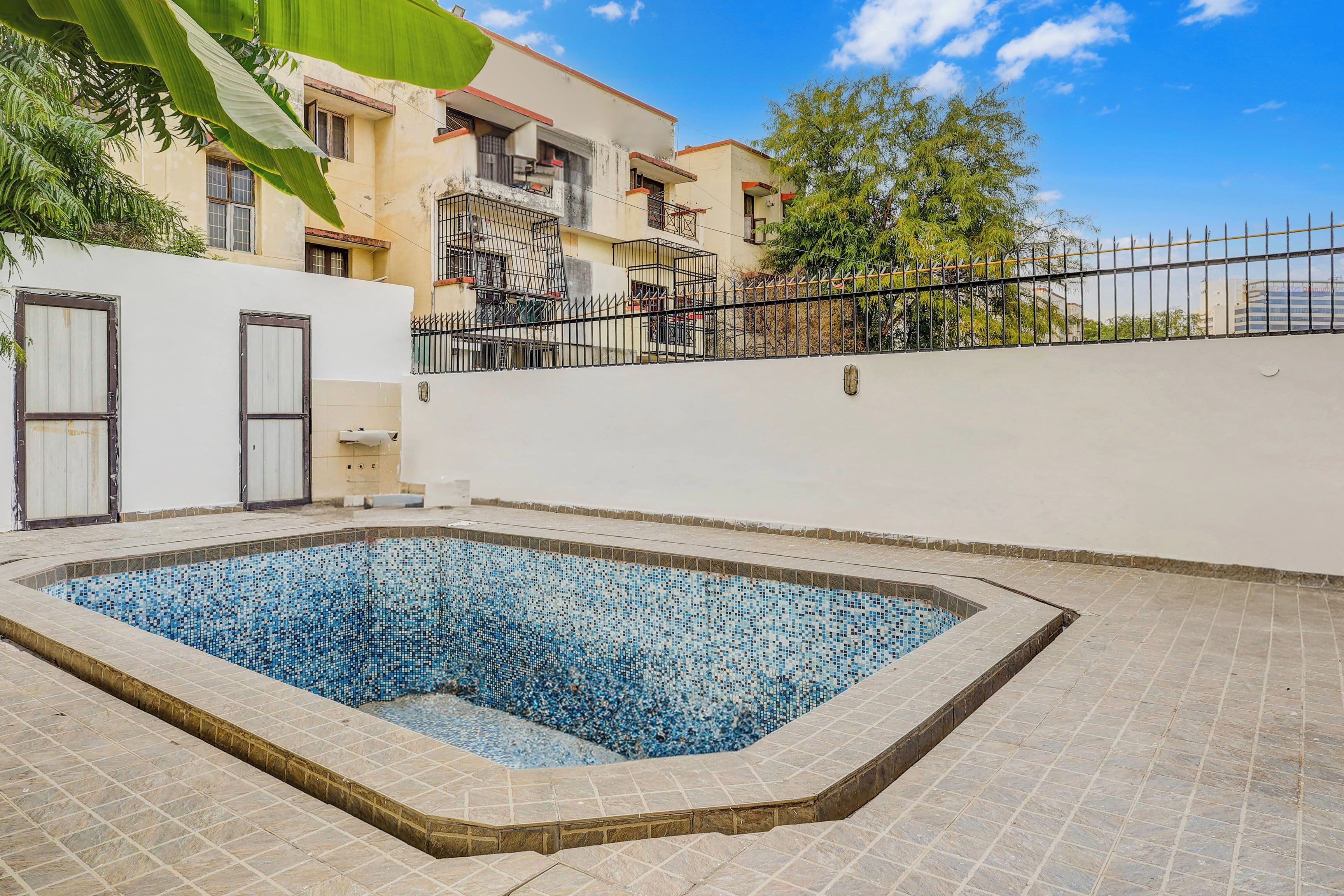 A swimming pool with tiled edges, surrounded by a low wall and a metal fence.