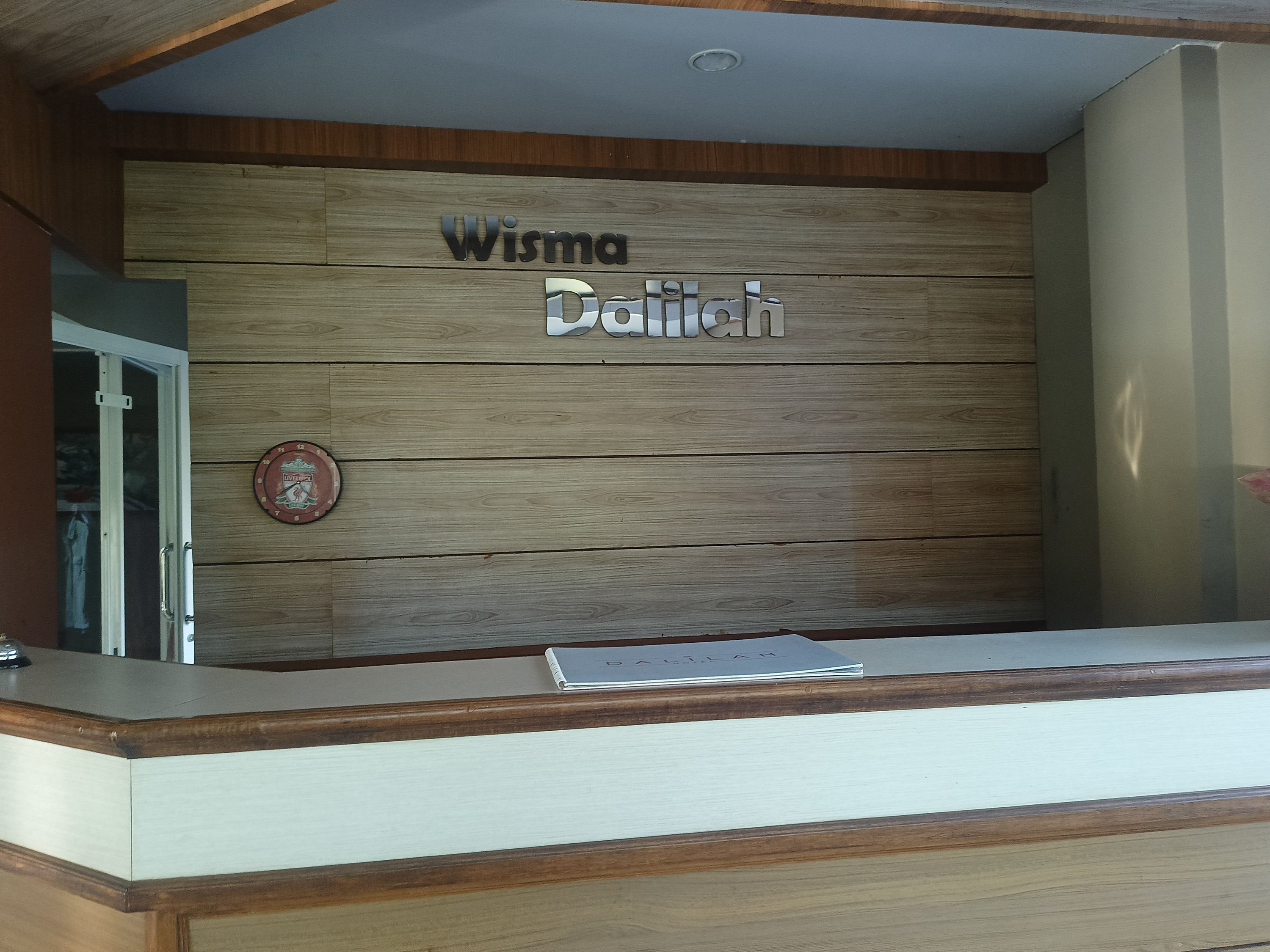 Una mesa de recepción con un panel de madera en la pared que muestra el nombre 'Wisma Datiyah'.
