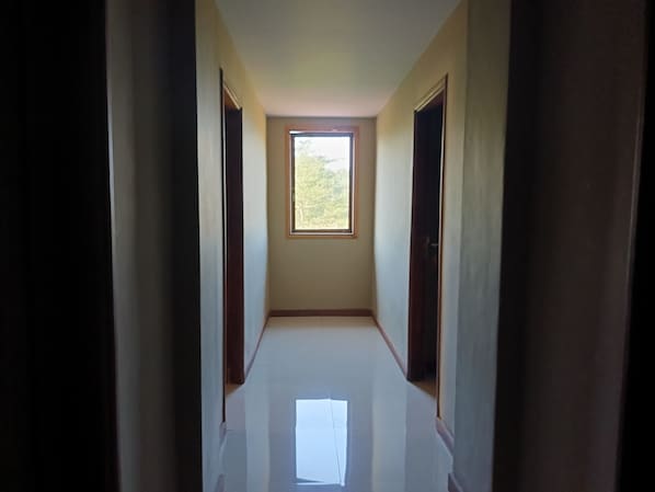 A narrow hallway with a window at the end, leading to a room. - Hotel O near Hasanuddin International Airport formerly Wisma Dalilah Syariah (Makassar)