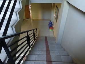 A staircase with a black metal railing, leading to a landing with a tiled floor and a blue vase. - Hotel O near Hasanuddin International Airport formerly Wisma Dalilah Syariah (Makassar)