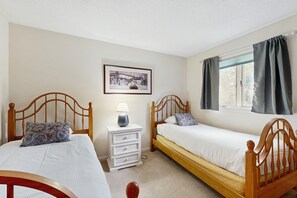 A bedroom with two wooden beds, a nightstand with a lamp, a framed picture on the wall, and a window with curtains. - 2BR at Nordic Village w/ shared pool, game room near ski, golf & storyland (Bartlett)