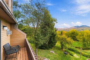 A wooden balcony with a view of a green landscape and hills. - 2BR at Nordic Village w/ shared pool, game room near ski, golf & storyland (Bartlett)