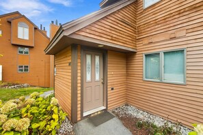 A two-story building with a brown wooden exterior, a front door with a glass panel, and a window with a closed shutter. - 2BR at Nordic Village w/ shared pool, game room near ski, golf & storyland (Bartlett)