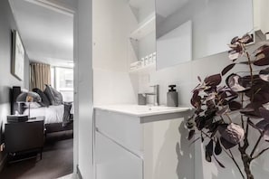 A modern bathroom with a white sink, mirror, and a plant. - Cozy City Studio by QV Market (Melbourne)