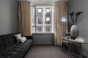 Een moderne woonkamer met een donkere bank, een klein rond tafeltje en een raam met gordijnen.