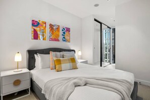 Una camera da letto moderna con un letto grande, lampade da comodino, un comodino e un'opera d'arte astratta alle pareti.