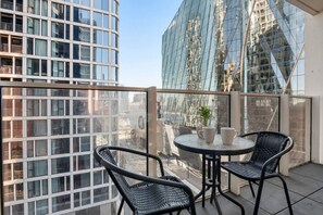 A balcony with a round table and two chairs, overlooking a cityscape with modern buildings. - Lovely Docklands 2 Bedroom (Docklands)