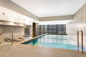 Ein moderner, überdachter Pool mit Glasbarriere, Liegestühlen und einer Wand mit Rasterstruktur.