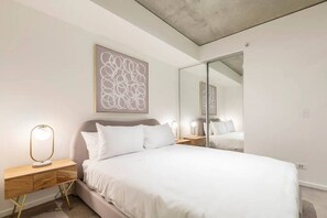 Quarto moderno com uma cama grande, mesas de cabeceira, uma obra de arte abstrata na parede e um espelho de corpo inteiro.