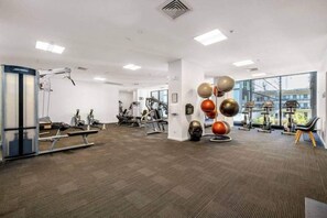 A gym with various exercise equipment, a wall-mounted ball rack, and large windows. - Cozy 1 Bedroom by Flagstaff (Melbourne)