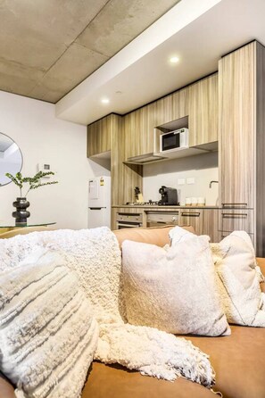 Een moderne woonkamer met een bank, kussens en een keuken in de achtergrond.