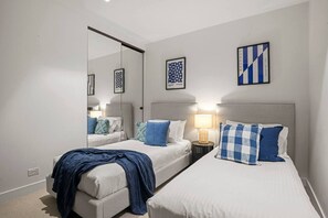 Habitació d'hotel amb dos llits, un mirall i una meseta de nit amb una làmpada.