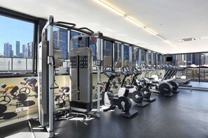 A gym with various exercise equipment, large windows, and a city view. - Lovely 2 Bedroom with Parking (Docklands)