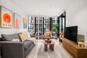 A modern living room with a sofa, armchair, coffee table, and a TV. - Lovely 2 Bedroom with Parking (Docklands)