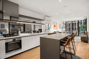 Une cuisine moderne dotée d’un îlot central, d’appareils électroménagers en acier inoxydable et d’une grande fenêtre offrant une vue sur la ville.