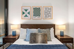 Une chambre d’hôtel comprenant un lit, deux tables de chevet, deux lampes et trois œuvres d’art encadrées accrochées au mur.