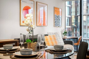 A dining area with a table set for four, a sofa, and a window with a view. - Lovely 2 Bedroom with Parking (Docklands)