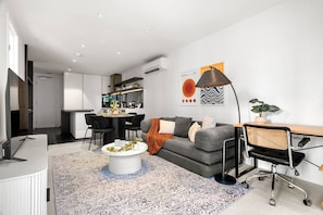 A modern living room with a grey sofa, a round coffee table, and a dining area with a black table and chairs. - Marvel Stadium 2 Bedroom (Docklands)