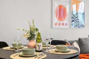 A dining table set with plates, glasses, and a bottle of wine, surrounded by chairs and a vase of flowers. - Marvel Stadium 2 Bedroom (Docklands)