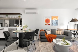 Ein modernes Wohnzimmer mit einem grauen Sofa, schwarzen Sesseln, einem Couchtisch und einem Essbereich mit einem runden Tisch.
