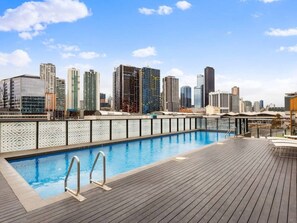 A rooftop pool with a city skyline view, wooden deck, and a decorative fence. - Docklands 2 Bedroom with Pool (Docklands)