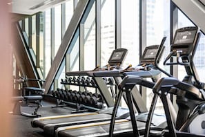 Ein Fitnessraum mit Laufbändern, Kurzhanteln und einer Bank.