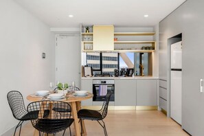 A compact kitchen with a dining area, modern appliances, and a view of a building. - Central 2 Bedroom with Sauna (Melbourne)