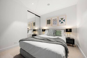 A modern bedroom with a large bed, bedside tables with lamps, a mirror, and framed artwork on the wall. - Chic 2 Bedroom near Marvel (Docklands)