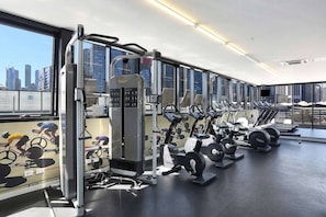 A gym with various exercise equipment, large windows, and a city view. - Chic 2 Bedroom near Marvel (Docklands)