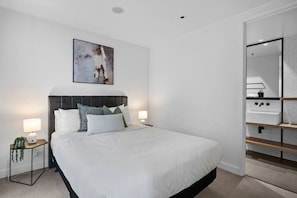 A modern bedroom with a large bed, two bedside tables with lamps, a headboard, and a painting above the bed. - Gorgeous 2 Bedroom by Marvel (Docklands)