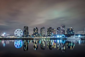 A nighttime city skyline with illuminated buildings and a Ferris wheel reflecting on the water. - Luxury Penthouse by Marvel (Docklands)