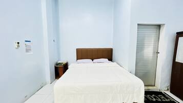 Quarto pequeno com uma cama de solteiro, cabeceira de madeira, mesa de cabeceira e porta com puxador de metal.