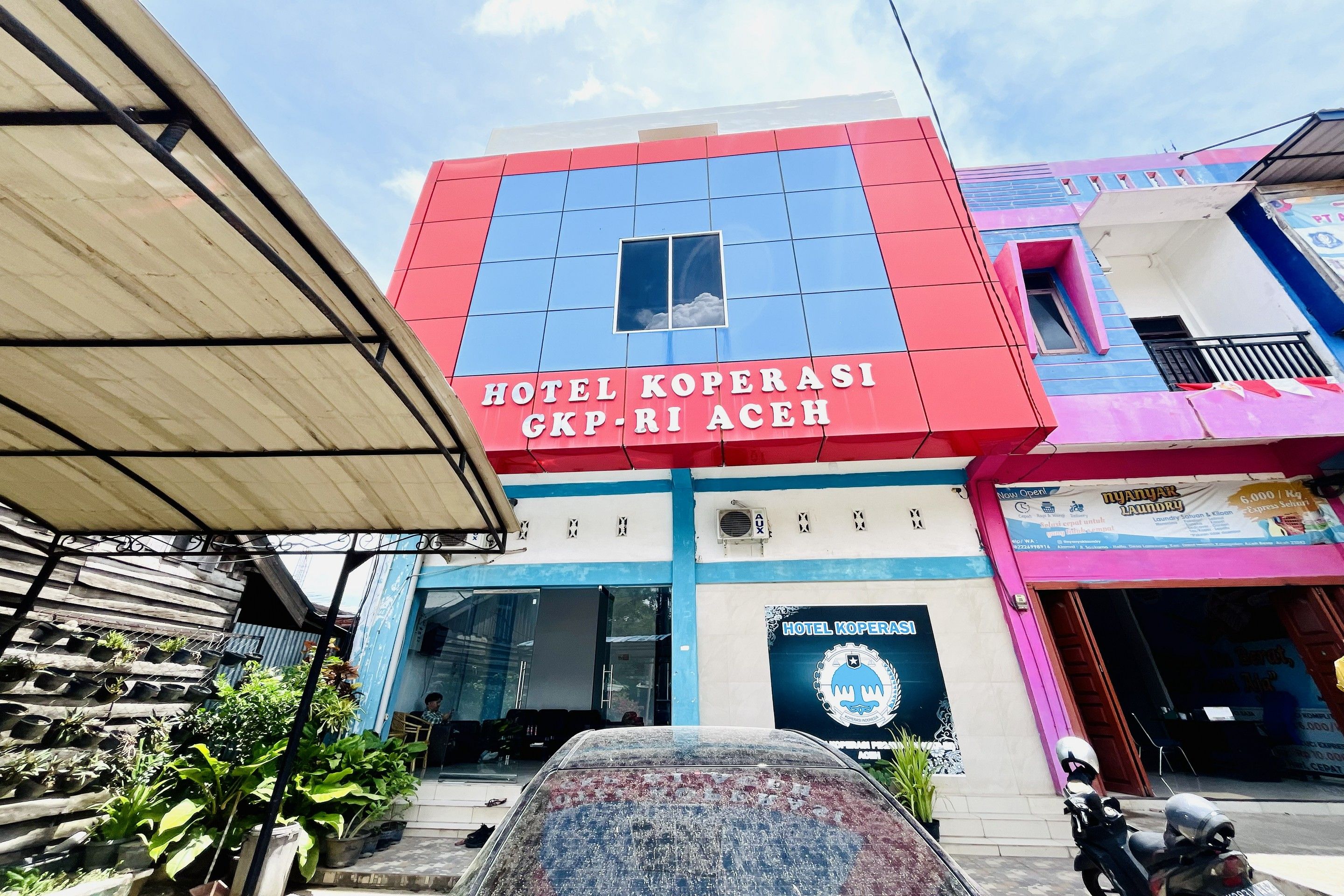 Um edifício com uma placa indicando 'HOTEL KOPERASI GKP-RI ACEH' e o logotipo de 'HOTEL KOPERAS'.