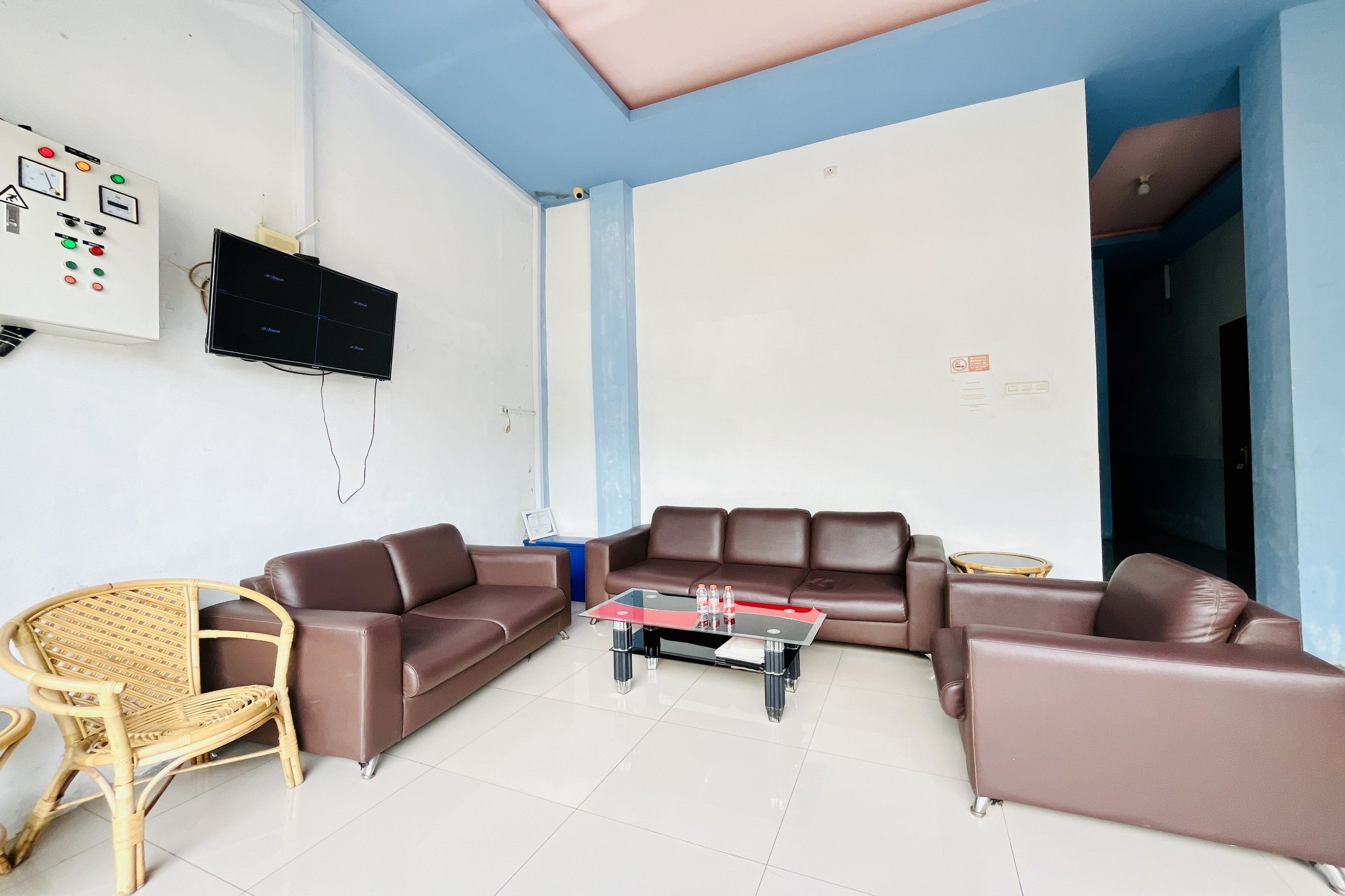 A living room with a brown leather sofa, a glass coffee table, a wicker chair, and a television mounted on the wall.