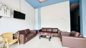 A living room with a brown leather sofa, a glass coffee table, a wicker chair, and a television mounted on the wall.