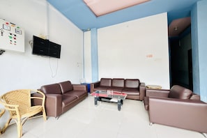 A living room with a brown leather sofa, a glass coffee table, a wicker chair, and a television mounted on the wall.