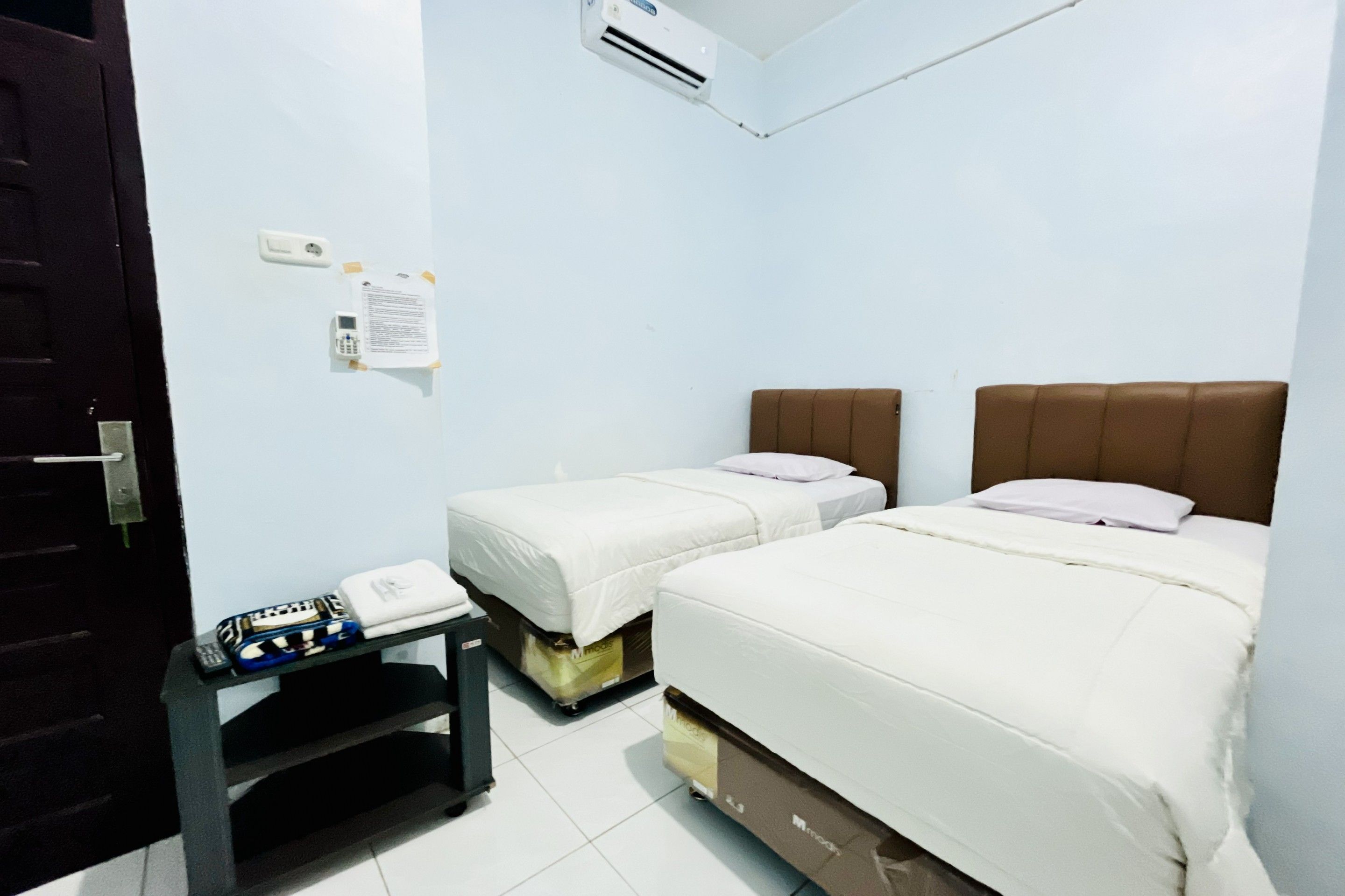 A hotel room with two beds, a desk with a telephone, and an air conditioning unit on the wall.