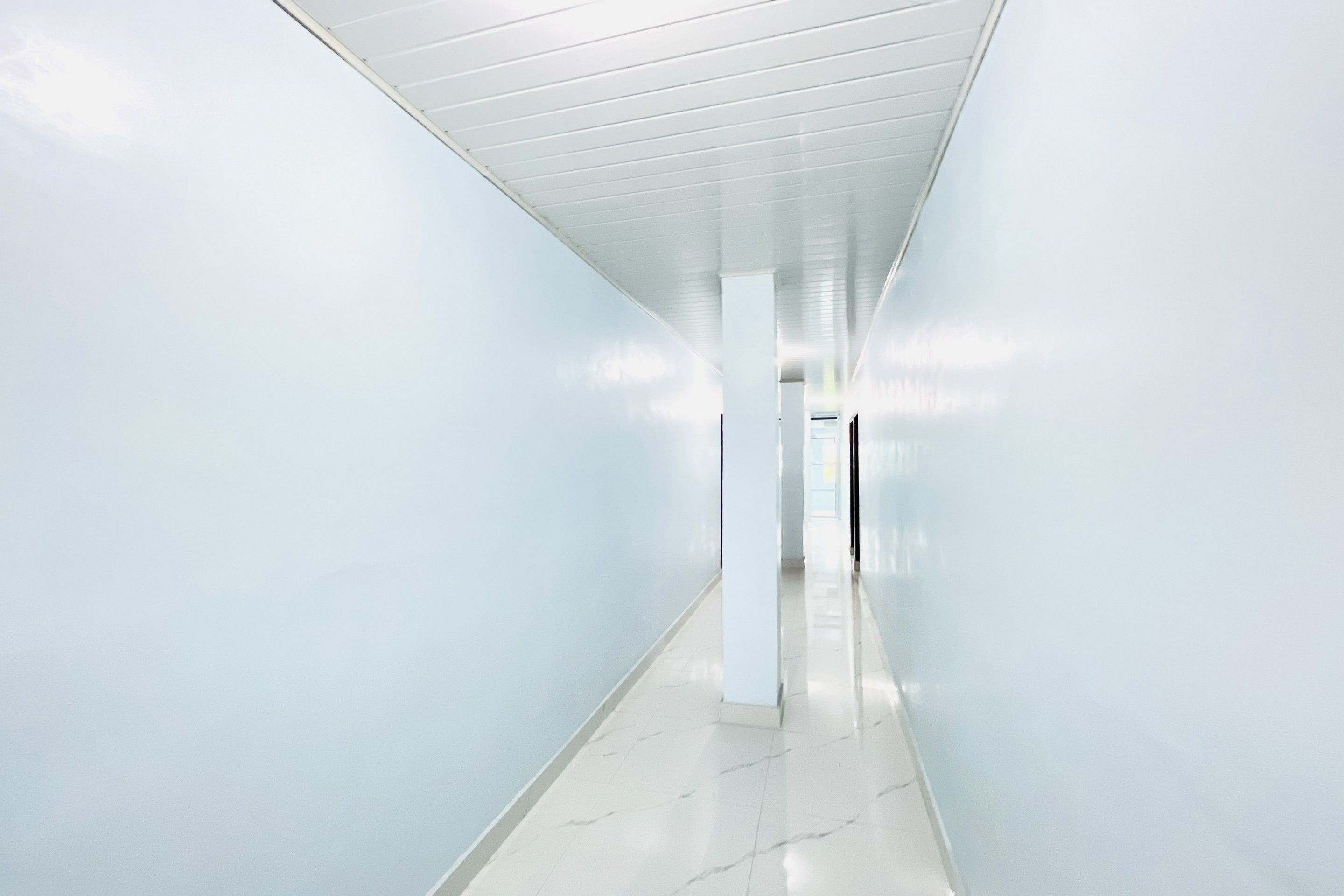 A long, narrow hallway with white walls and a tiled floor.