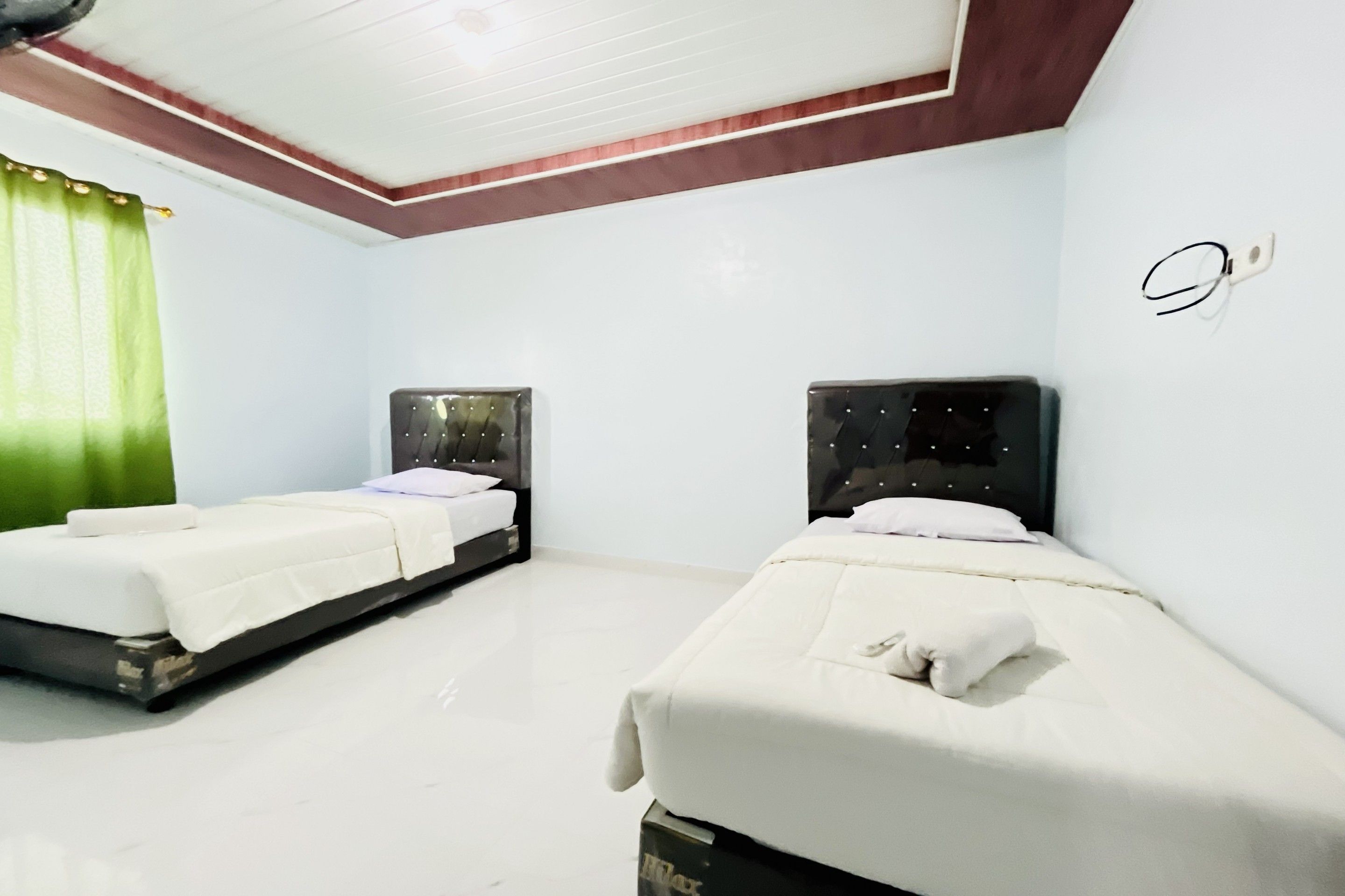 A hotel room with two single beds, a green curtain, and a white ceiling.
