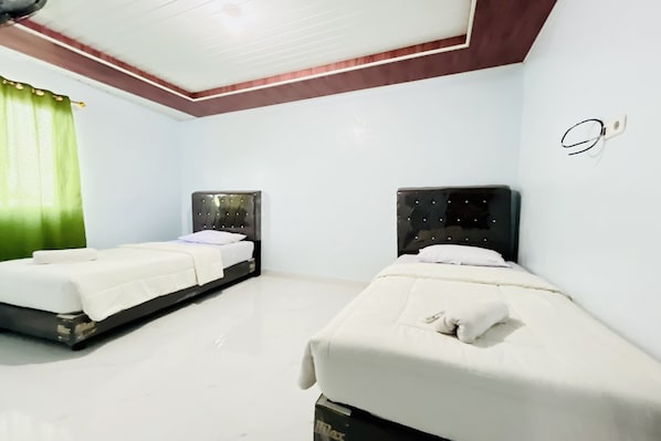 A hotel room with two single beds, a green curtain, and a white ceiling.