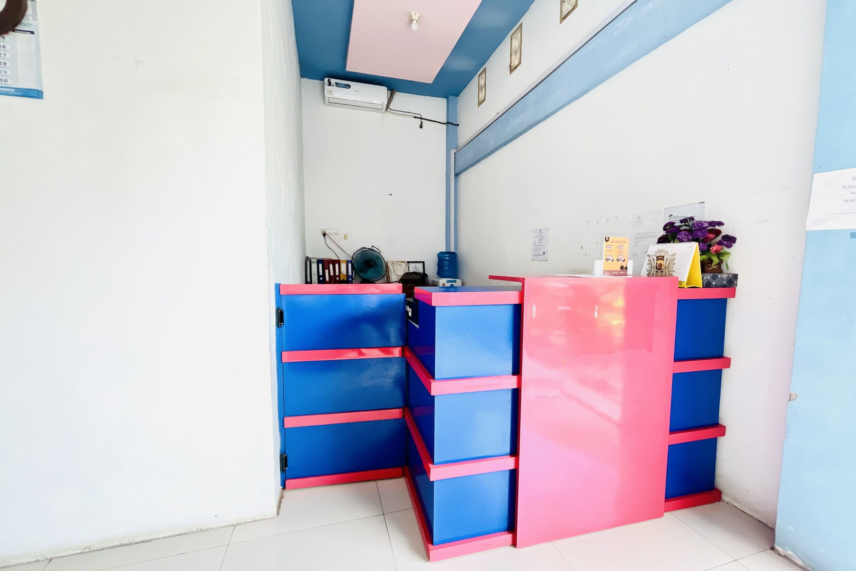 A reception desk with blue and pink drawers, a water dispenser, and a fan.