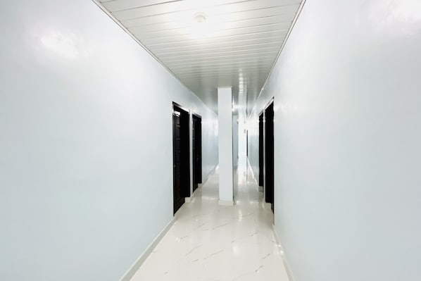 A corridor with white walls and a shiny floor, leading to a door at the end.