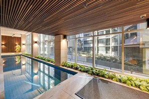 Une piscine intérieure dotée d’un plafond en bois, de grandes fenêtres et offrant une vue sur l’extérieur.