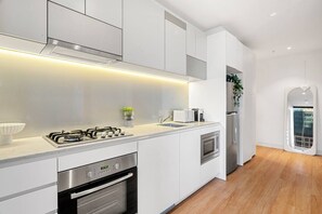 A modern kitchen with white cabinetry, stainless steel appliances, and a wooden floor. - Skyline Oasis 3 Bedroom (Melbourne)