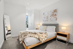 Quarto moderno com cama grande, mesa de cabeceira e espelho.