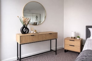 A bedroom with a wooden bedside table, a bedside lamp, and a bed with a grey headboard. - Marvel Stadium View 2 Bedroom (Docklands)
