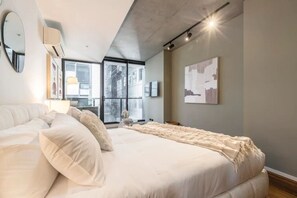 Et moderne soveværelse med en stor seng, en sofa og et vindue med udsigt over byen.
